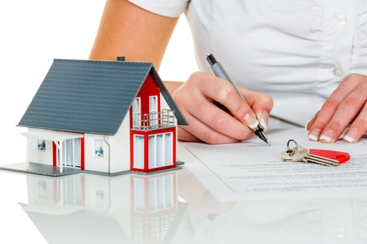 Produto financeiro: Home Equity - Uma casa vermelha e branca ao lado de uma mão assinando um contato