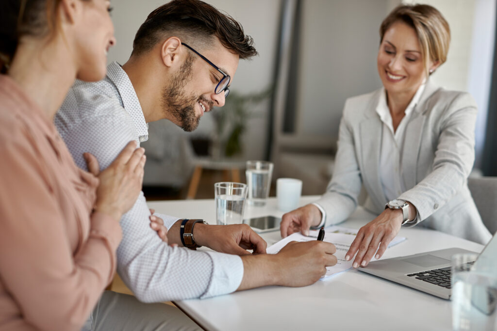 Uma profissional sentada na mesa negociando seguros com um casal feliz