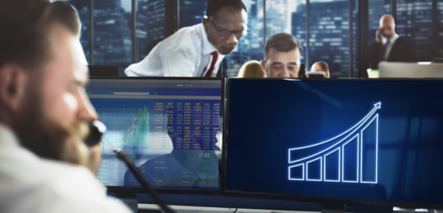 Três homens em um escritório, com um deles em foco, falando no telefone e observando gráficos e números no computador. Representando as diversas profissões no mercado financeiro